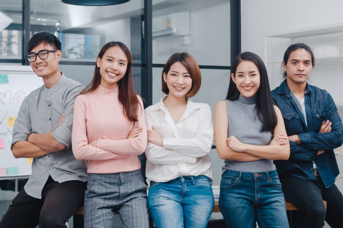Group of Asia young creative people in smart casual wear smiling and arms crossed in creative office workplace. Diverse Asian male and female stand together at startup. Coworker teamwork concept.
