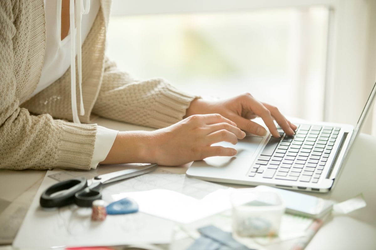 Hands printing on a laptop, sewing accessories around. Concept photo, side view, closeup, close-up