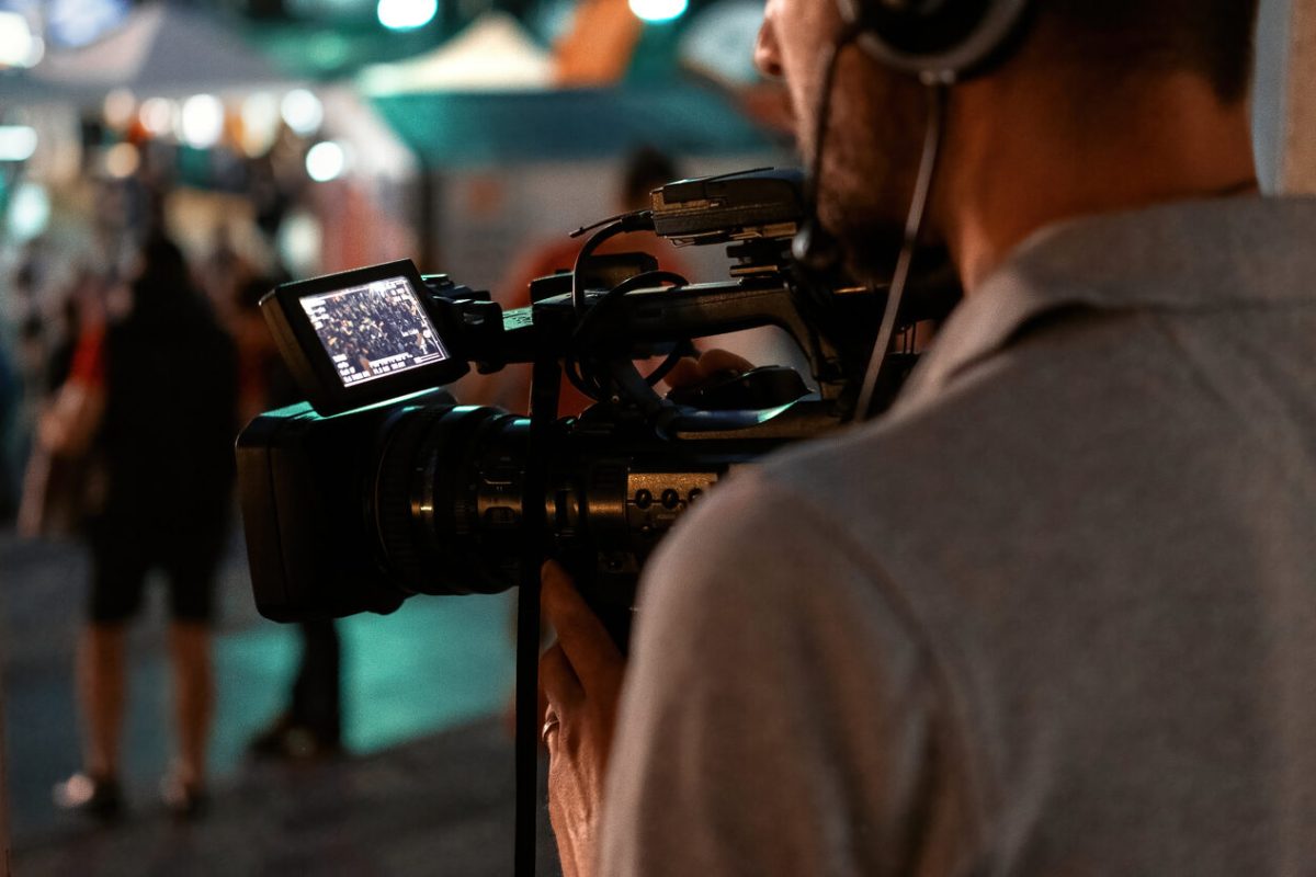 Professional cameraman recording poeple watching football in a public place at night