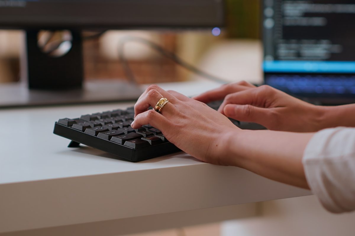 Professional software developer types code on a laptop in a sleek workspace. Asian female freelancer doing remote work on app development, software engineering and agile coding practices. Camera B.
