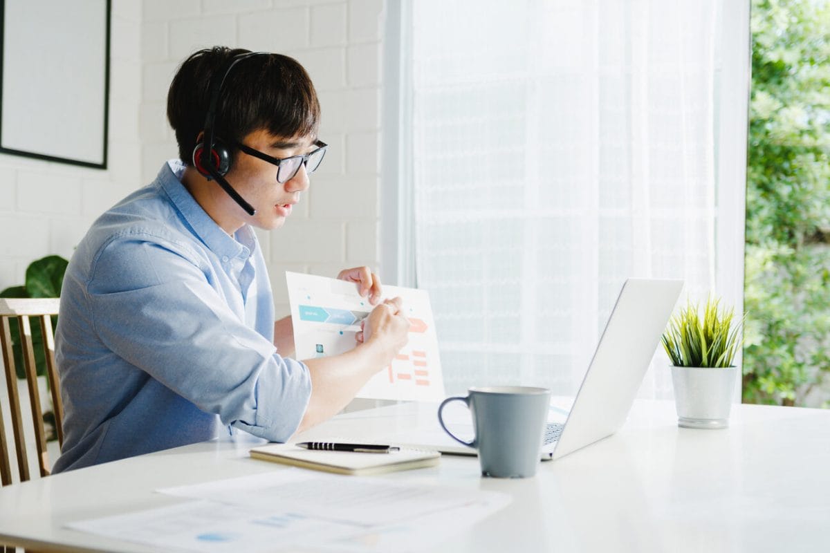 Young Asia businessman using laptop talk to colleagues about plan in video call while smart working from home at living room. Self-isolation, social distancing, quarantine for corona virus prevention.